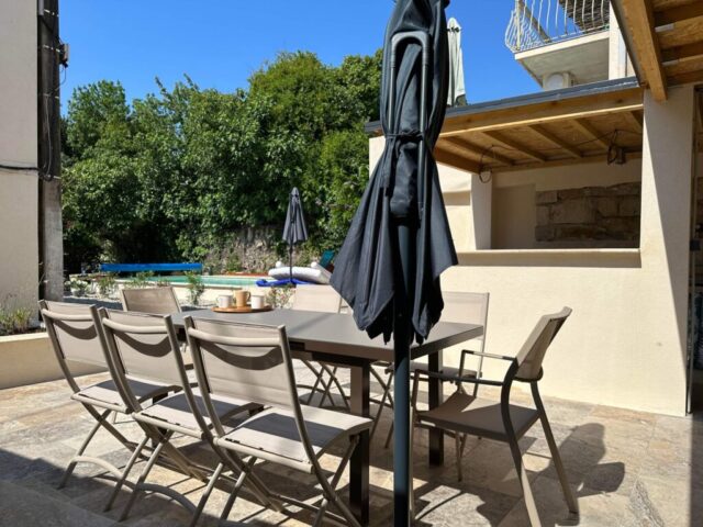 Terrasse extérieure du Mas du Camisard avec grande table à manger, parasol et vue sur la piscine, idéale pour repas en famille ou entre amis en Cévennes
