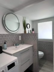 Salle de bain moderne avec vasque, miroir rond et machine à laver – gîte Le Mas du Camisard à Ribaute-les-Tavernes dans le Gard