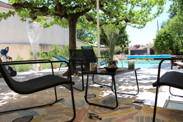 Espace détente sous les arbres, avec fauteuils et table basse face à la piscine du Mas du Camisard à Ribaute-les-Tavernes, ambiance apéritif à l’ombre