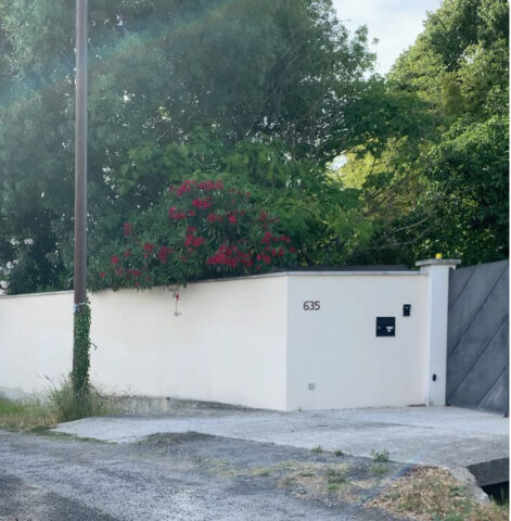 Vue de l'entrée principale du Mas du Camisard avec portail fermé, mur blanc, végétation méditerranéenne et accès privatif